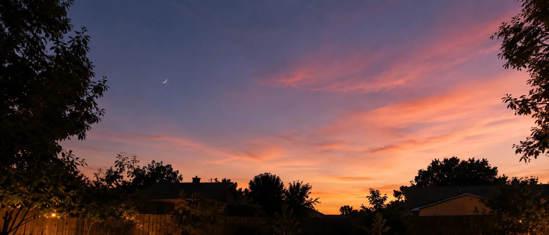 Warm suburban backyard at dusk with a glowing sunset sky and string lights in the trees