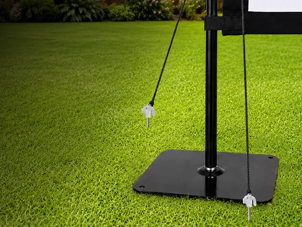 Close-up of STWUI projector screen steel base plate and ground stakes securing the stand on a grass lawn