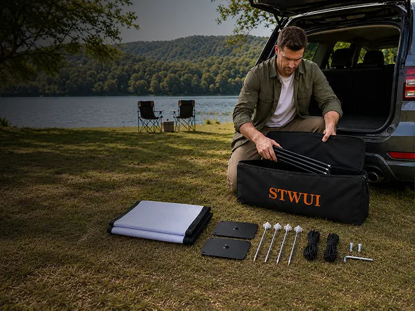 STWUI projector screen carry bag with screen, poles, base plates, stakes, and ropes laid out at a lakeside campsite