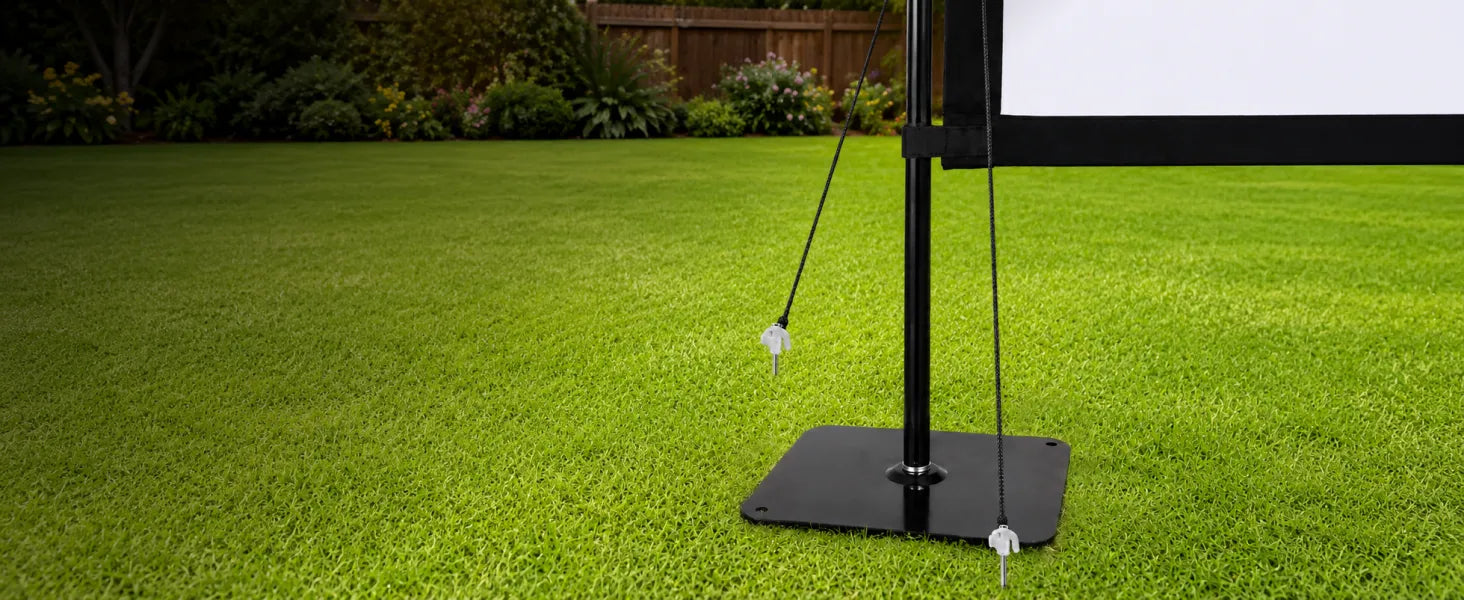 STWUI projector screen upgraded base plate with ground stakes and wind ropes anchored on a backyard lawn